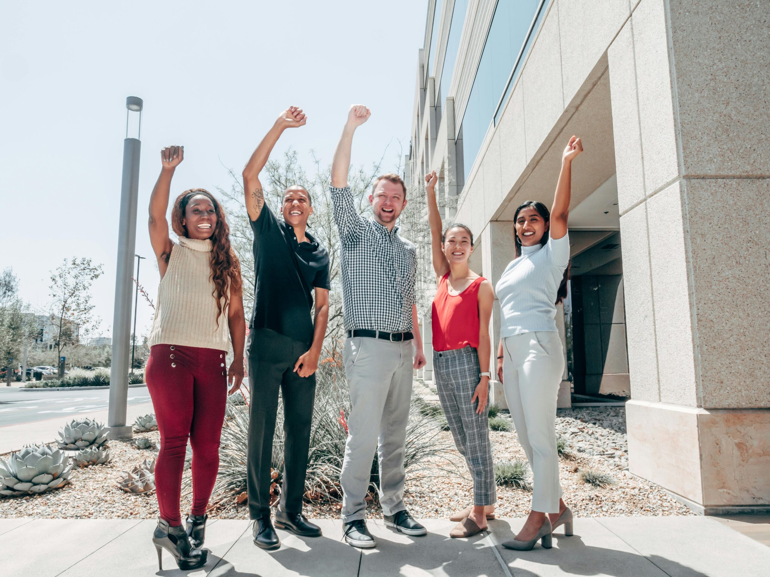 pexels-kindelmedia-7688665 Group of five diverse people standing outdoors raising their fists in celebration